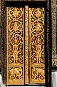 Wat Xieng Thong temple in Luang Prabang, Laos. Detail of a wooden door of the sim with gilded carvings on a red background. 